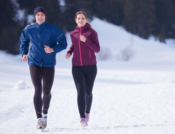 Zwei Personen laufen in Sportkleidung auf verschneitem Weg in winterlicher Landschaft.