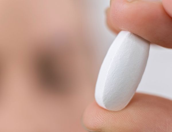 Hand hält eine weiße Antibiotika-Kapsel auf neutralem Hintergrund.