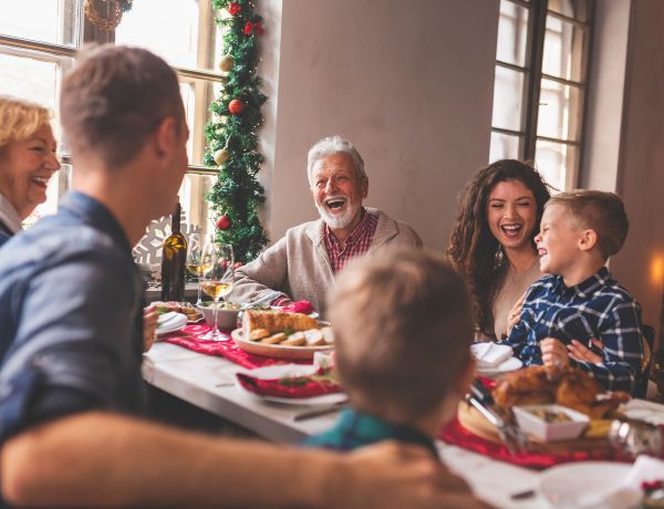 Familie sitzt an festlich gedecktem Tisch und feiert gemeinsames Weihnachtsessen.