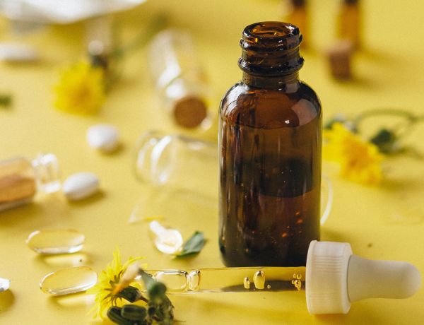 Braune Medizinflasche mit Pipette auf gelbem Hintergrund, symbolisiert pflanzliche Tropfen.