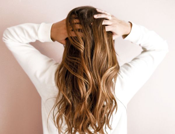 Frau mit langen braunen Haaren steht mit dem Rücken zur Kamera und hält sie zusammen.