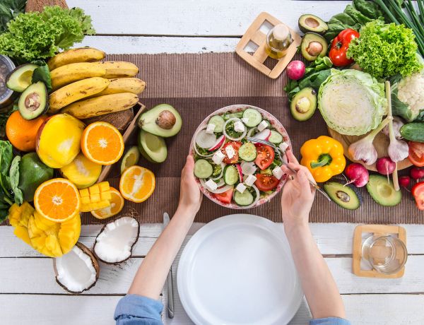 Draufsicht auf gedeckten Tisch mit Schüssel Salat, umgeben von Obst, Avocados und verschiedenem Gemüse.