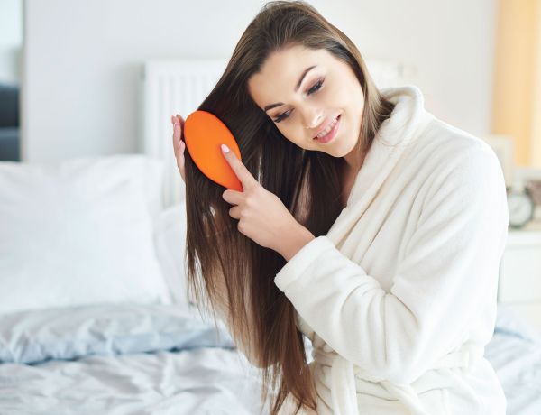 Frau mit langen Haaren sitzt auf dem Bett und kämmt sich.