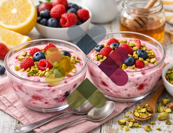 Zwei Glasschalen mit rosa Müsli, Beeren und gehackten Pistazien, daneben Honigglas und Zitrone.