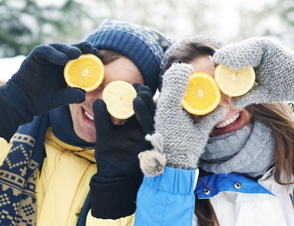 Zwei Personen halten sich Zitronenscheiben vor die Augen, Winterkleidung und Schnee im Hintergrund.