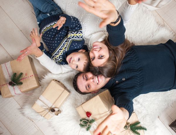 Drei Personen liegen auf dem Boden zwischen verpackten Geschenken und schauen nach oben.