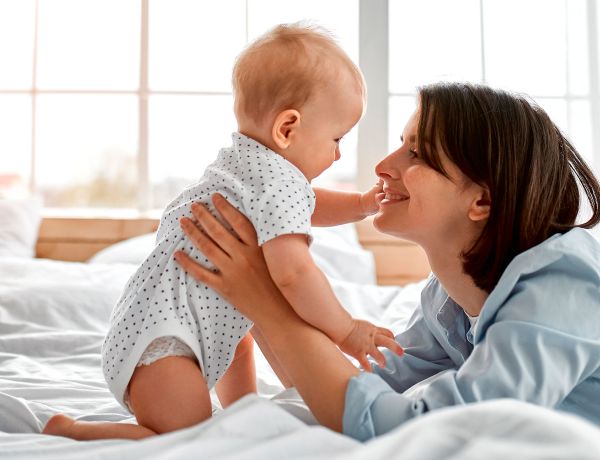 Mutter spielt im Bett mit ihrem Baby, beide lachen fröhlich.