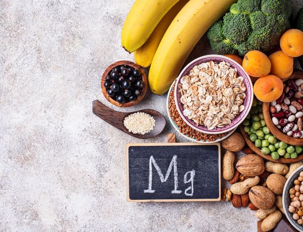 Verschiedene magnesiumreiche Lebensmittel wie Nüsse, Bananen, Kakao und Trockenfrüchte auf grauem Untergrund.