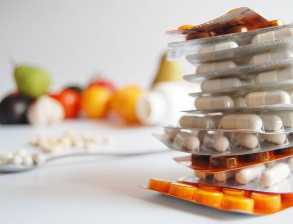 Glas mit verschiedenen Nahrungsergänzungskapseln und Obst im Hintergrund als Symbol für Gesundheit.