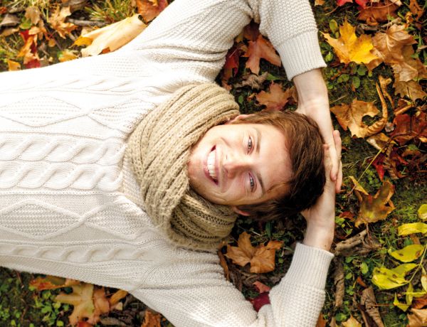 Mann liegt im Herbstlaub und lächelt, Symbol für starke Abwehrkräfte.