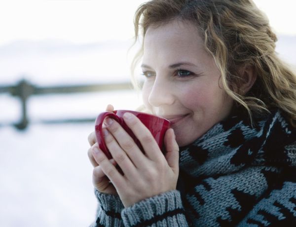 Frau mit Schal hält eine rote Tasse in den Händen, winterliche Landschaft im Hintergrund.
