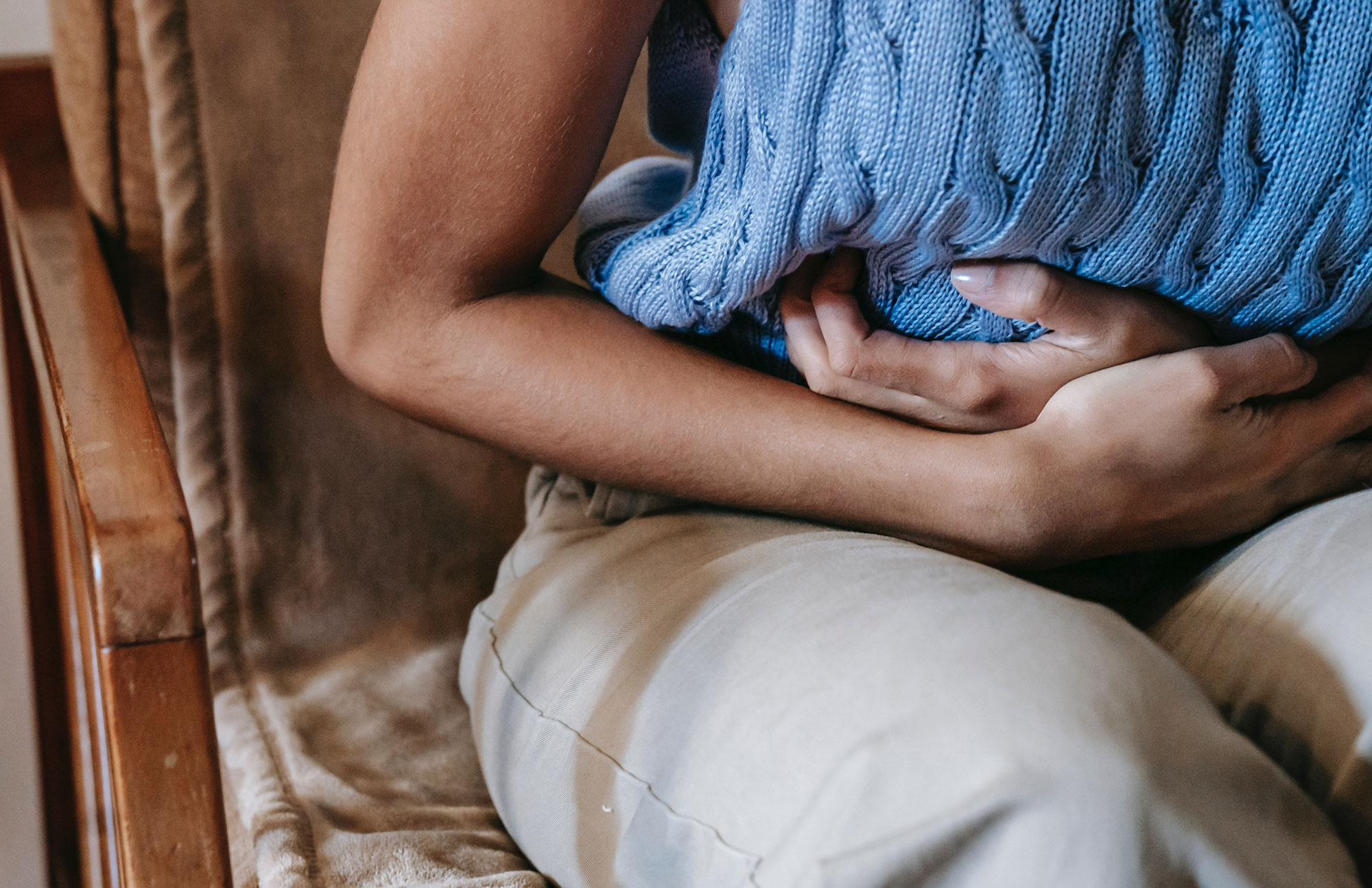 Frau hält sitzend beide Hände auf den Bauch als Zeichen für Verdauung und Bauchschmerzen