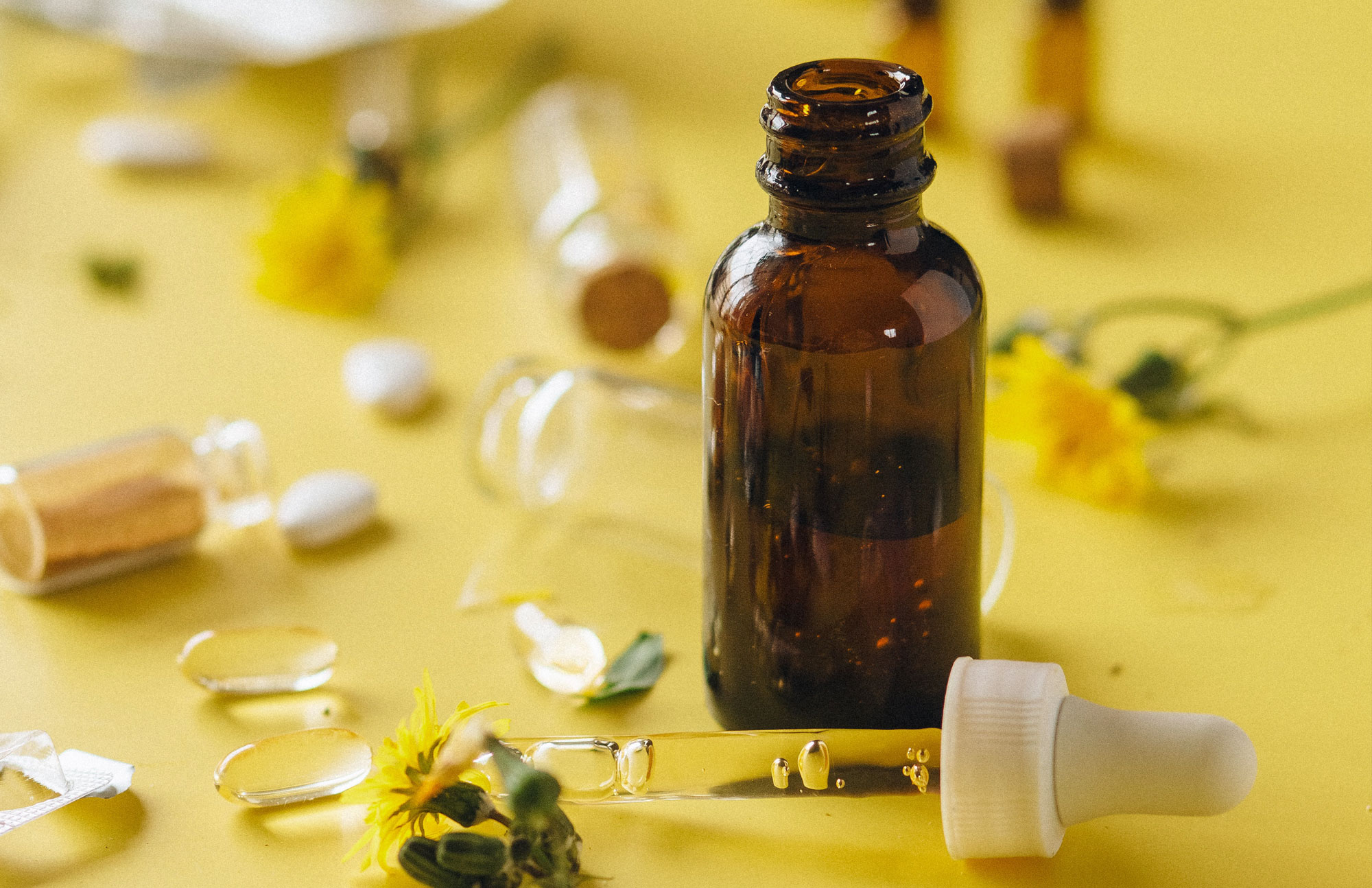 Braune Medizinflasche mit Pipette auf gelbem Hintergrund, symbolisiert pflanzliche Tropfen.