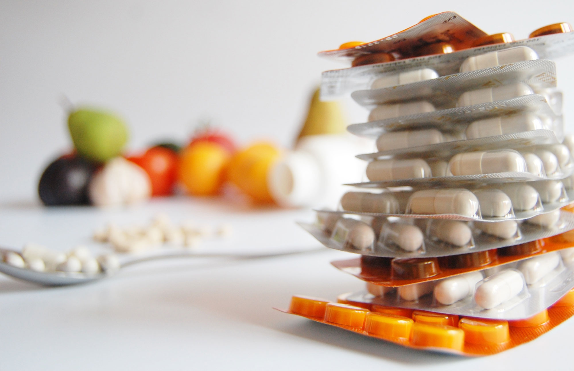 Glas mit verschiedenen Nahrungsergänzungskapseln und Obst im Hintergrund als Symbol für Gesundheit.