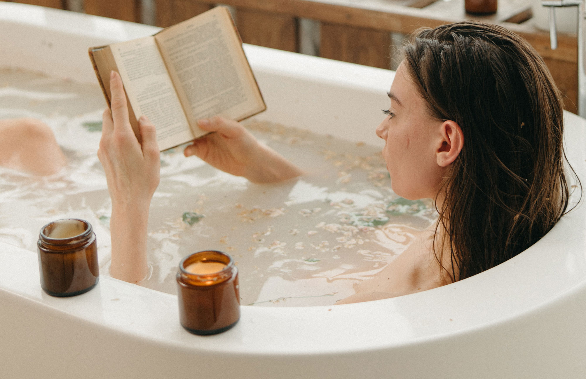 Frau liegt entspannt in einer Badewanne und liest ein Buch