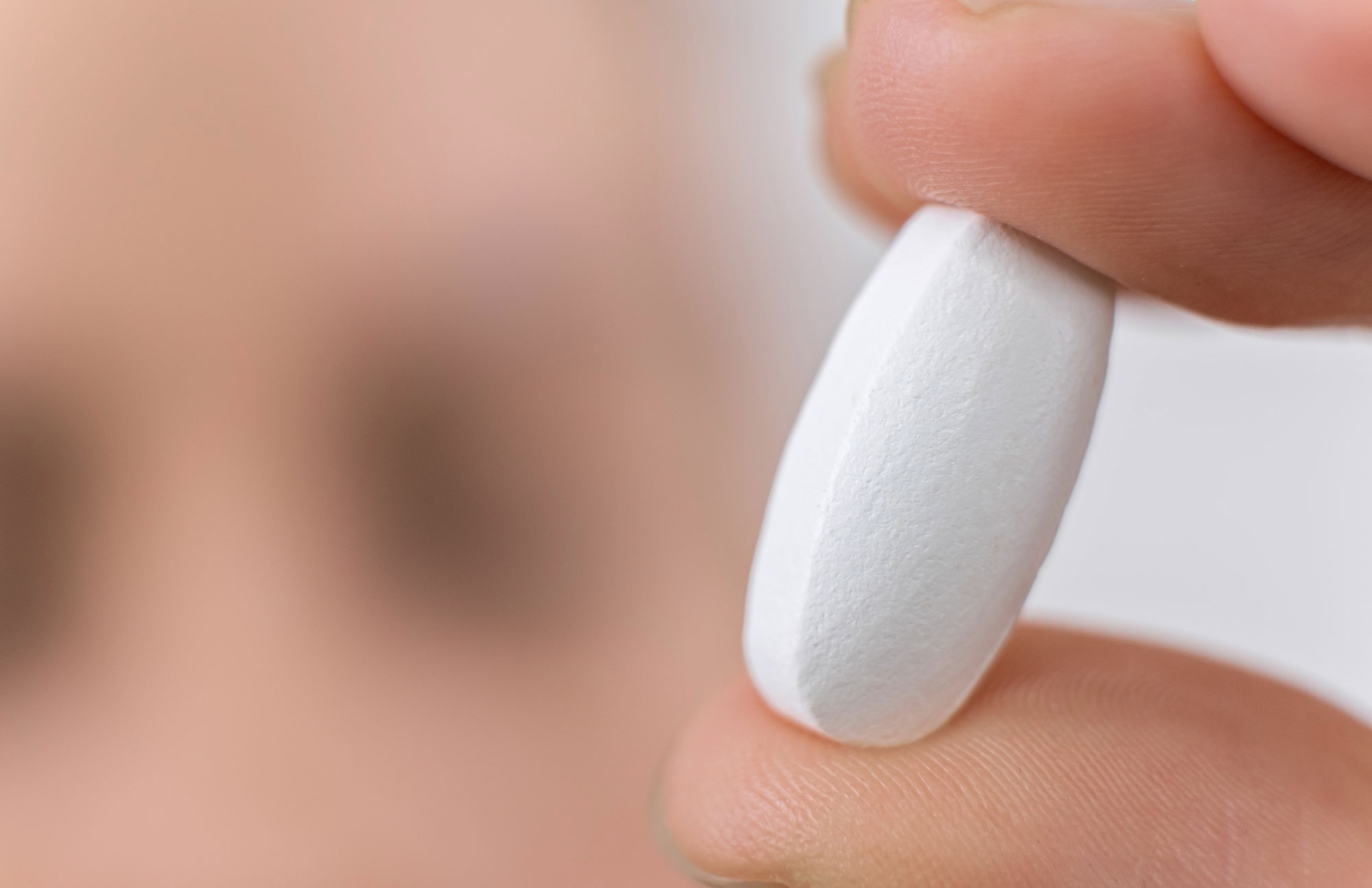 Hand hält eine weiße Antibiotika-Kapsel auf neutralem Hintergrund.