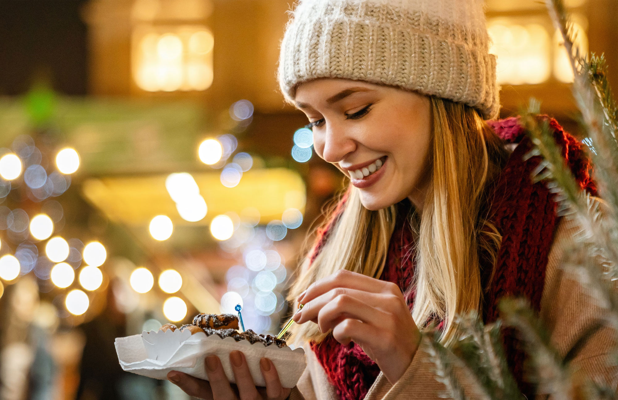 Frau probiert Süßes auf einem festlich dekorierten Weihnachtsmarkt.