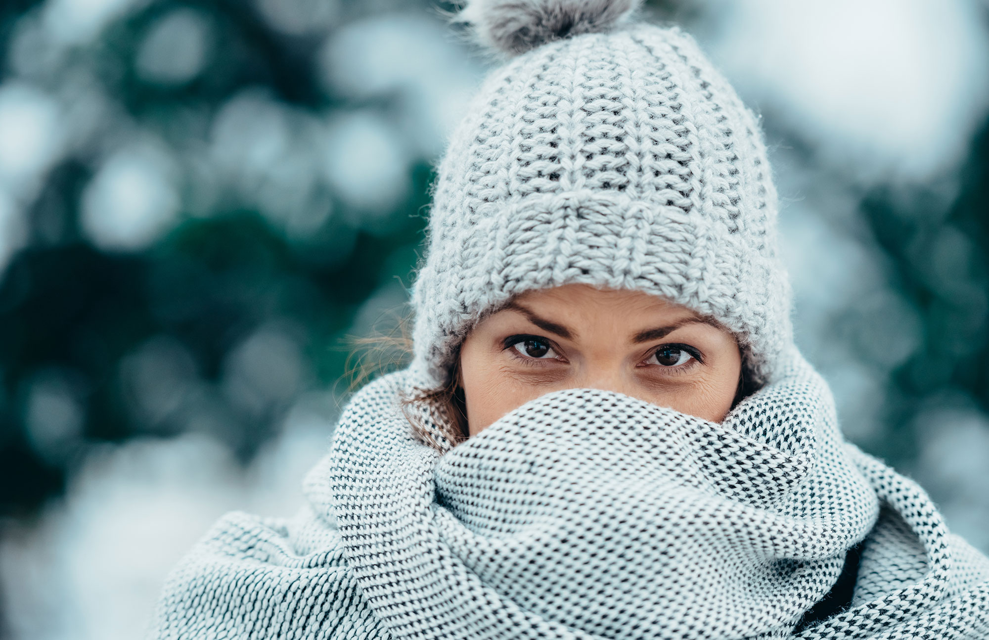 Frau trägt Schal und Mütze im Schnee, Symbol für Hautpflege im Winter.