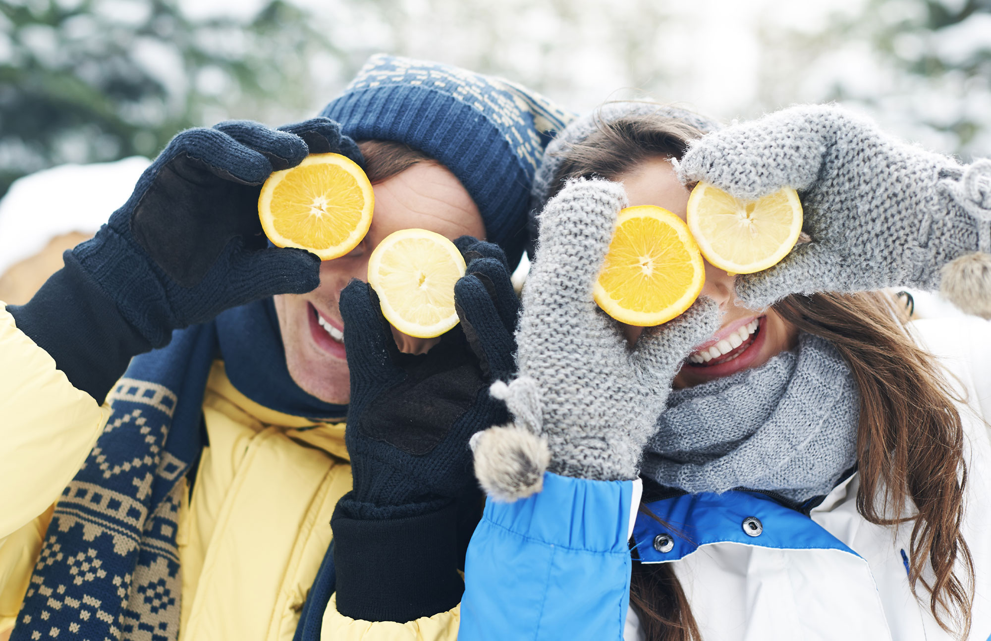 Zwei Personen halten sich Zitronenscheiben vor die Augen, Winterkleidung und Schnee im Hintergrund.