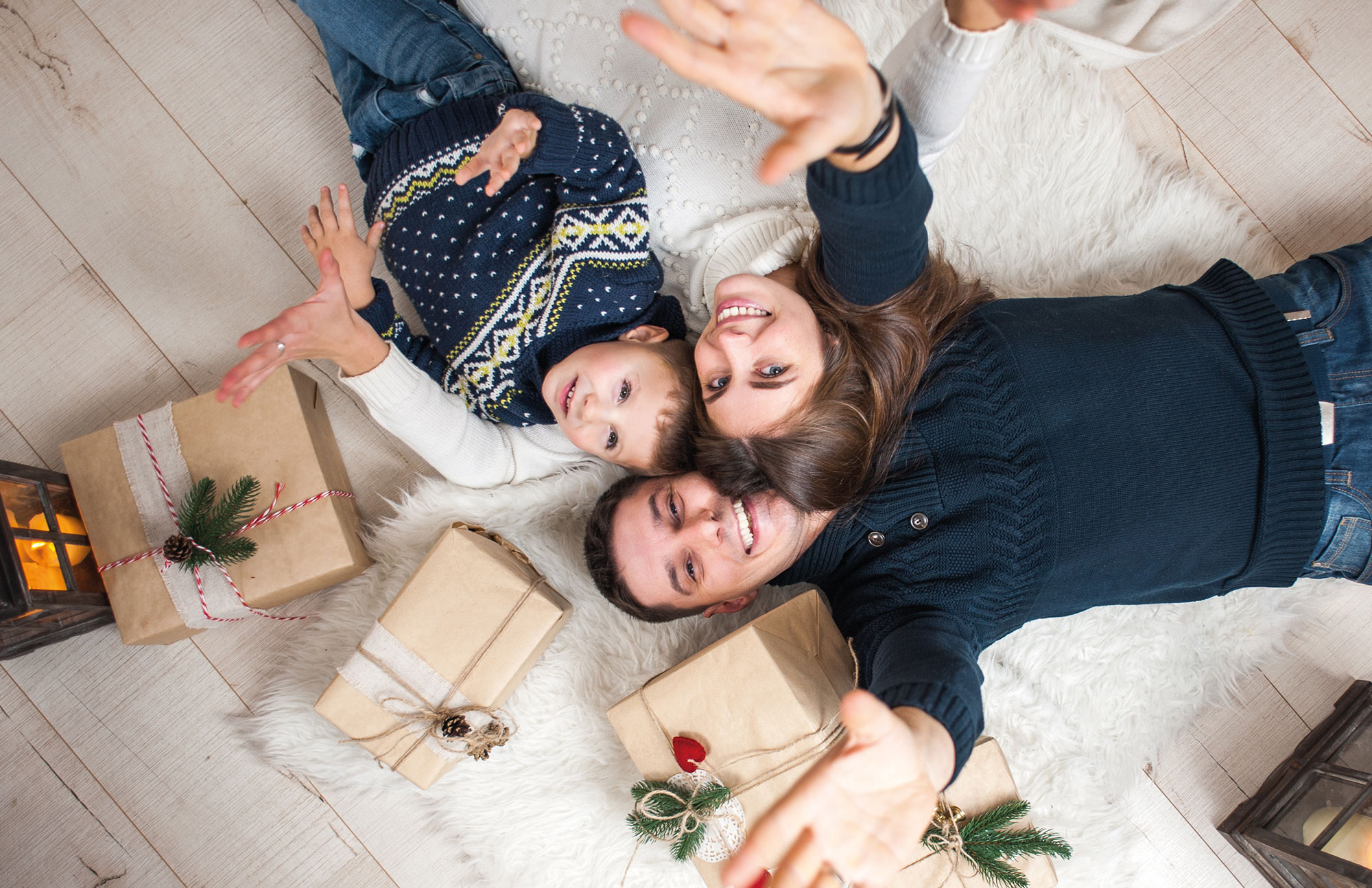 Drei Personen liegen auf dem Boden zwischen verpackten Geschenken und schauen nach oben.